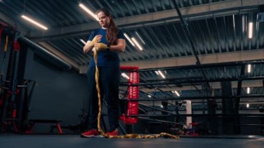 Güçlü kolları olan sportif kız sıkı bir idmana hazırlanıyor. Parmaklarını jimnastik salonunda korumak için yumruklarına bandaj yapıştırıyor.