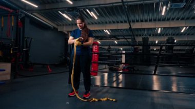Güçlü kolları olan sportif kız sıkı bir idmana hazırlanıyor. Parmaklarını jimnastik salonunda korumak için yumruklarına bandaj yapıştırıyor.