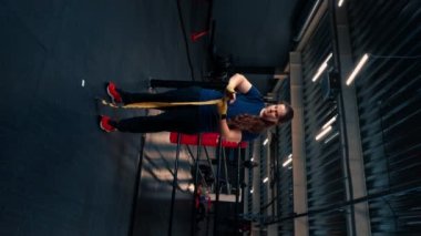 Dikey video. Güçlü kolları olan sporcu kız sıkı bir antrenmana hazırlanıyor. Parmaklarını spor salonunda korumak için yumruklarına bandaj yapıştırıyor.