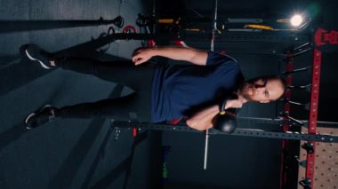 Spordan sonra spor salonundaki sporcunun dikey video portresi. Bir adam elinde kettlebell tutarak sportif bir yaşam stili ister.