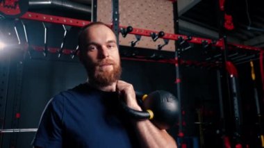 Spor salonunda spor yaptıktan sonra tatmin olmuş bir sporcunun portresi. Bir adam elinde kettlebell tutarak sportif bir yaşam tarzı ister.