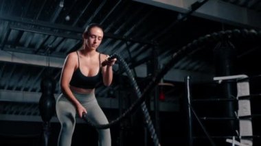 Vücut geliştirme yarışması motivasyonuna hazırlanmak için spor salonunda elinde iple egzersiz yapan genç ve güzel bir fitness kadını.
