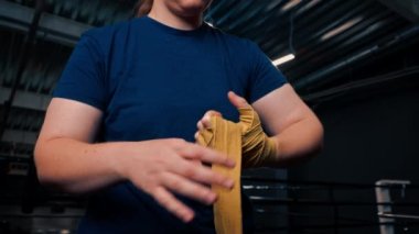 Güçlü kolları olan sportif kız sıkı bir idmana hazırlanıyor. Yumruklarını bandajla sarıyor. Parmaklarını jimnastik salonunda koruyor.