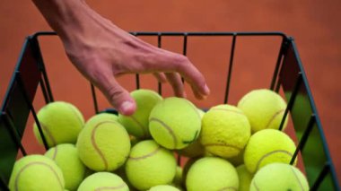 Tenis antrenmanı ya da tenis kortu müsabakasına başlamak için sepetten tenis topu alan bir elin yakın çekimi