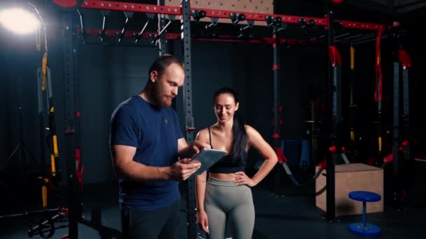男性トレーナーはタブレットを手に持って 競技のために体を準備する女性アスリートにトレーニングスケジュールを示します — ストック動画