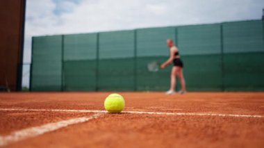 Sahada uzanan tenis topuna yakın plan çekimde oyuncu elinde raketle antrenman yapıyor.