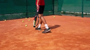 Tenis oyuncusu ya da koç, maç sonrası spor ekipmanları ile kortta bir tüple tenis topları toplar.