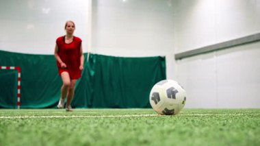 Genç bayan futbolcu kız, yeşil sentetik çimen futbolu sahası tekmeleme antrenmanında pas veriyor.