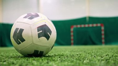 Siyah-beyaz bir futbol topu, spor maçı başlamadan önce yeşil sentetik çimlerin üzerinde bir spor sahasında uzanır.