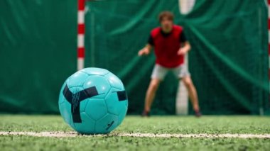 Kalecinin kalesine gol atmak için futbol sahasında topa tekme atan bir futbolcunun yakın çekimi.