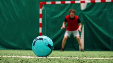 Kalecinin kalesine gol atmak için futbol sahasında topa tekme atan bir futbolcunun yakın çekimi.