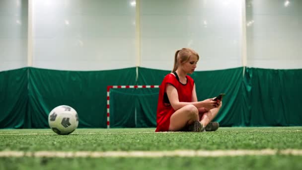 Düşünceli Kız Futbolcu Sentetik Çimlerin Üzerinde Oturmuş Elinde Telefonla Spor — Stok video
