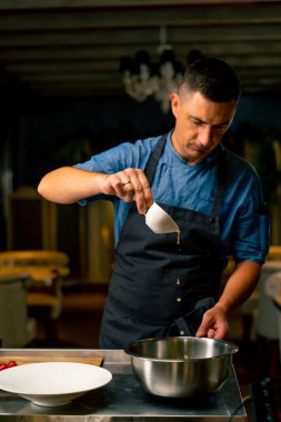 Bir İtalyan restoranında şef yemek hazırlarken bir kase salataya zeytinyağı döker.