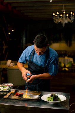 Bir İtalyan restoranının şefi profesyonel mutfakta salata hazırlarken malzemeleri kızartmak için gaz ocağı kullanır.