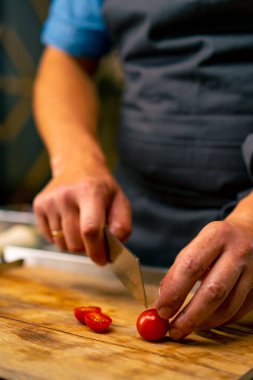 İtalyan bir şef profesyonel mutfakta salata hazırlarken kiraz domateslerini bıçakla kesiyor.