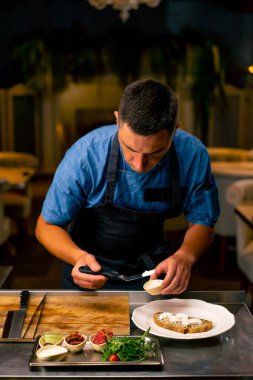 İtalyan restoranında profesyonel bir mutfakta bruschetta hazırlarken ekmeğe krem peynir döken bir şefin yakın çekimi.