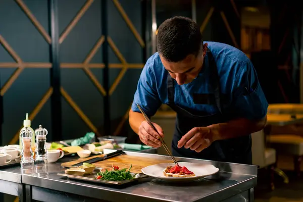İtalyan restoranındaki profesyonel bir mutfakta biftek avokado ve domatesli bruschetta hazırlayan bir şefin yakın çekimi.