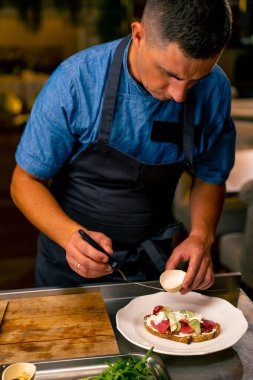 İtalyan restoranındaki profesyonel bir mutfakta biftek avokado ve domatesli bruschetta hazırlayan bir şefin yakın çekimi.
