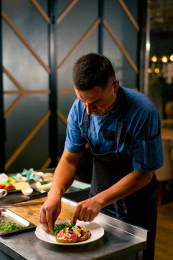 İtalyan restoranındaki profesyonel bir mutfakta biftek avokado ve domatesli bruschetta hazırlayan bir şefin yakın çekimi.