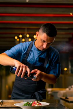 Şef bir şişe balzamik sirke tutuyor ve İtalyan restoranının mutfağında salata hazırlıyor.