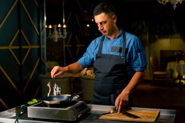 İtalyan restoranının profesyonel mutfağında elinde maşayla domuz pastırması kızartan bir şefin yakın çekimi.