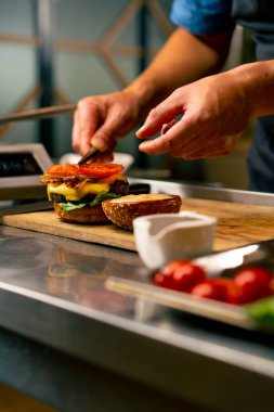 İtalyan restoranının profesyonel mutfağında köfteli ve sebzeli ve peynirli burger hazırlayan bir şefin yakın çekimi.