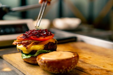 İtalyan restoranının profesyonel mutfağında köfteli ve sebzeli ve peynirli burger hazırlayan bir şefin yakın çekimi.