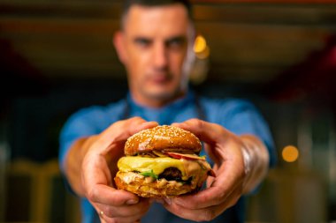 Üniformalı İtalyan restoranının şefi profesyonel mutfağında pişirdiği burgeri gösteriyor.