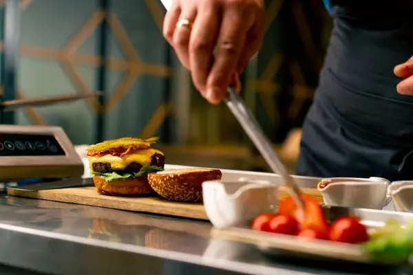 A close-up of a chef preparing a burger with beef patty with vegetables and cheese in the professional kitchen of Italian restaurant