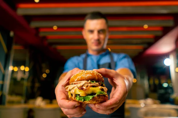 The chef of Italian restaurant in uniform shows the burger he cooked in his professional kitchen