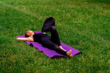 Aktif, güzel Yogi kadın antrenmandan sonra şehir parkında dinleniyor spor paspasına uzanmış gökyüzüne bakıyor.