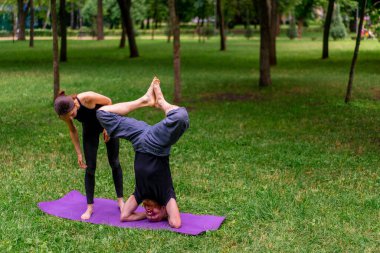 Kadın yoga eğitmeni, parktaki bir adamla birlikte temiz hava alanında bir ders veriyor. Manevi egzersizler yapıyor.