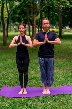 Şehir parkında yoga yapan bir çiftin portresi namaste hareketleriyle meditasyon egzersizleri yapıyor insanlar zihinsel ve ruhsal sağlığa odaklanıyor.