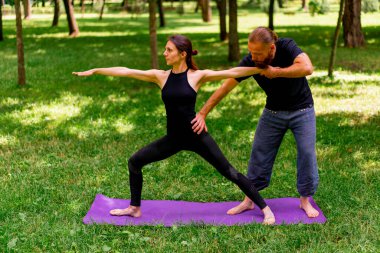 Erkek yoga hocası, parkta bir kadınla birlikte, temiz hava ile ilgili bir ders veriyor. Çift, manevi egzersizler yapıyor.