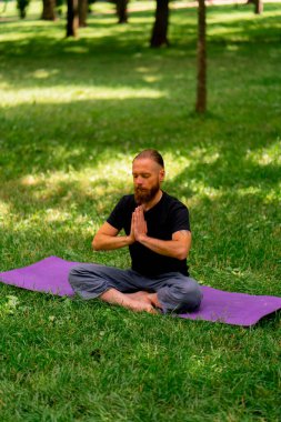 Yakışıklı sakallı adam parkta meditasyon yapıyor. Lotus pozisyonunda oturuyor. Yoga yapıyor.