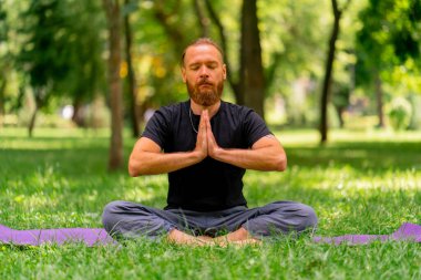Yakışıklı sakallı adam parkta meditasyon yapıyor. Lotus pozisyonunda oturuyor. Yoga yapıyor.