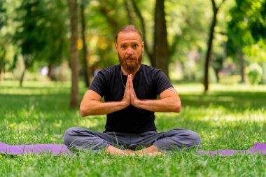 Yakışıklı sakallı adam parkta meditasyon yapıyor. Lotus pozisyonunda oturuyor. Yoga yapıyor.