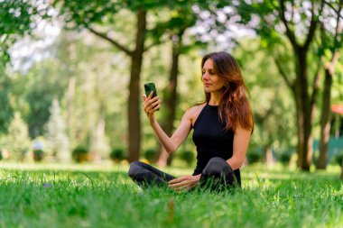 Eğitimden önce ya da sonra parkta yürüyüş yaparken elinde akıllı telefonu tutan aktif, güzel bir Yogi kadını.