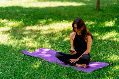 Eğitimden önce ya da sonra parkta yürüyüş yaparken elinde akıllı telefonu tutan aktif, güzel bir Yogi kadını.