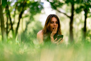 Eğitimden önce ya da sonra parkta dinlenen aktif, güzel bir Yogi kadını spor minderinde yatarken akıllı telefon görüşmesiyle konuşuyor.