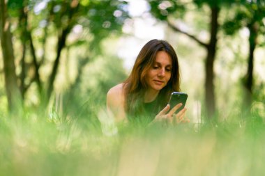 Eğitimden önce ya da sonra parkta dinlenen aktif, güzel bir Yogi kadını spor minderinde yatarken akıllı telefon görüşmesiyle konuşuyor.