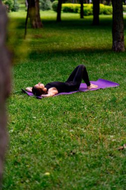 Aktif, güzel Yogi kadın antrenmandan sonra şehir parkında dinleniyor spor paspasına uzanmış gökyüzüne bakıyor.