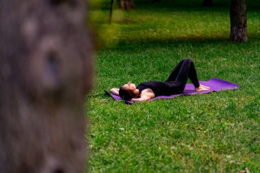 Aktif, güzel Yogi kadın antrenmandan sonra şehir parkında dinleniyor spor paspasına uzanmış gökyüzüne bakıyor.