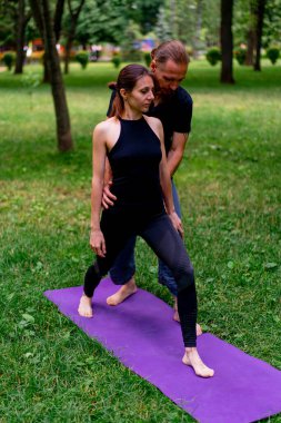 Erkek yoga hocası, parkta bir kadınla birlikte, temiz hava ile ilgili bir ders veriyor. Çift, manevi egzersizler yapıyor.