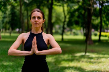 Deneyimli bir kadın eğitmen parkta meditasyon yapar yoga yapar ve farklı kas grupları çalıştırır.