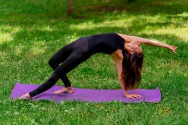 Deneyimli bir kadın eğitmen parkta meditasyon yapar yoga yapar ve farklı kas grupları çalıştırır.