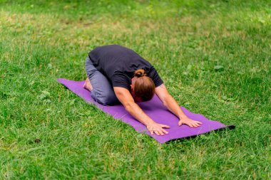 Yakışıklı sakallı adam parkta meditasyon yapıyor yoga yapıyor esneme hareketleri yapıyor ve farklı kas grupları çalıştırıyor.