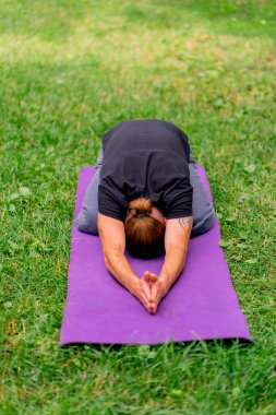 Yakışıklı sakallı adam parkta meditasyon yapıyor yoga yapıyor esneme hareketleri yapıyor ve farklı kas grupları çalıştırıyor.