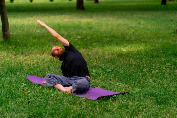 handsome bearded man meditating in the park practicing yoga doing stretching and exercises different muscle groups