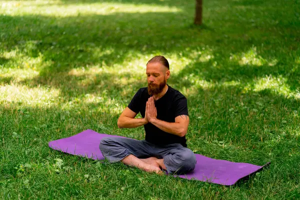 portrait handsome bearded man meditating in the park sitting in lotus position practicing yoga zen healthy lifestyle calm meditation
